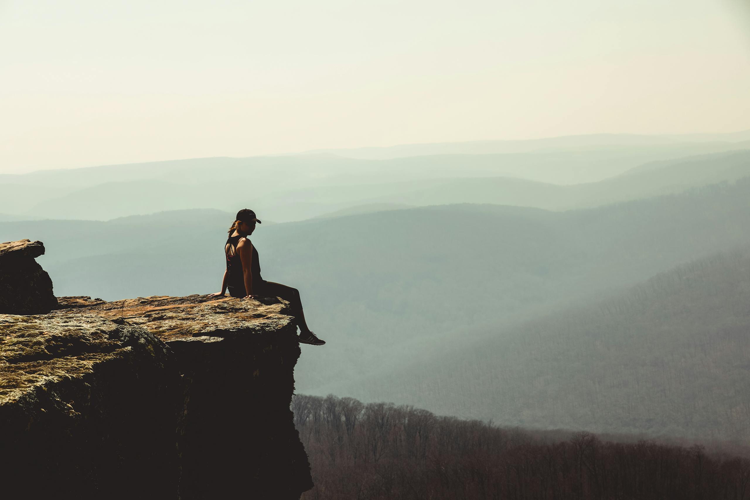 Woman sitting on a cliff edge overlooking a vast mountain landscape in Arkansas.